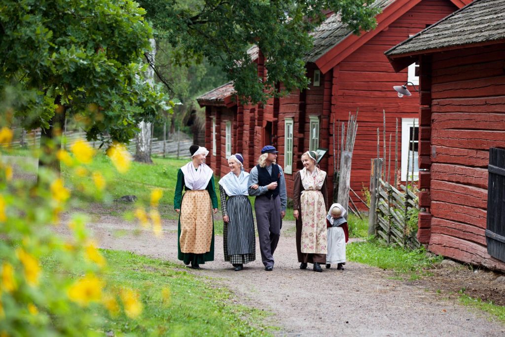 Barn, vuxna och äldre i tidsenliga kläder på Vallby Friluftsmuseum i Västerås. Fotograf: Laila Duran