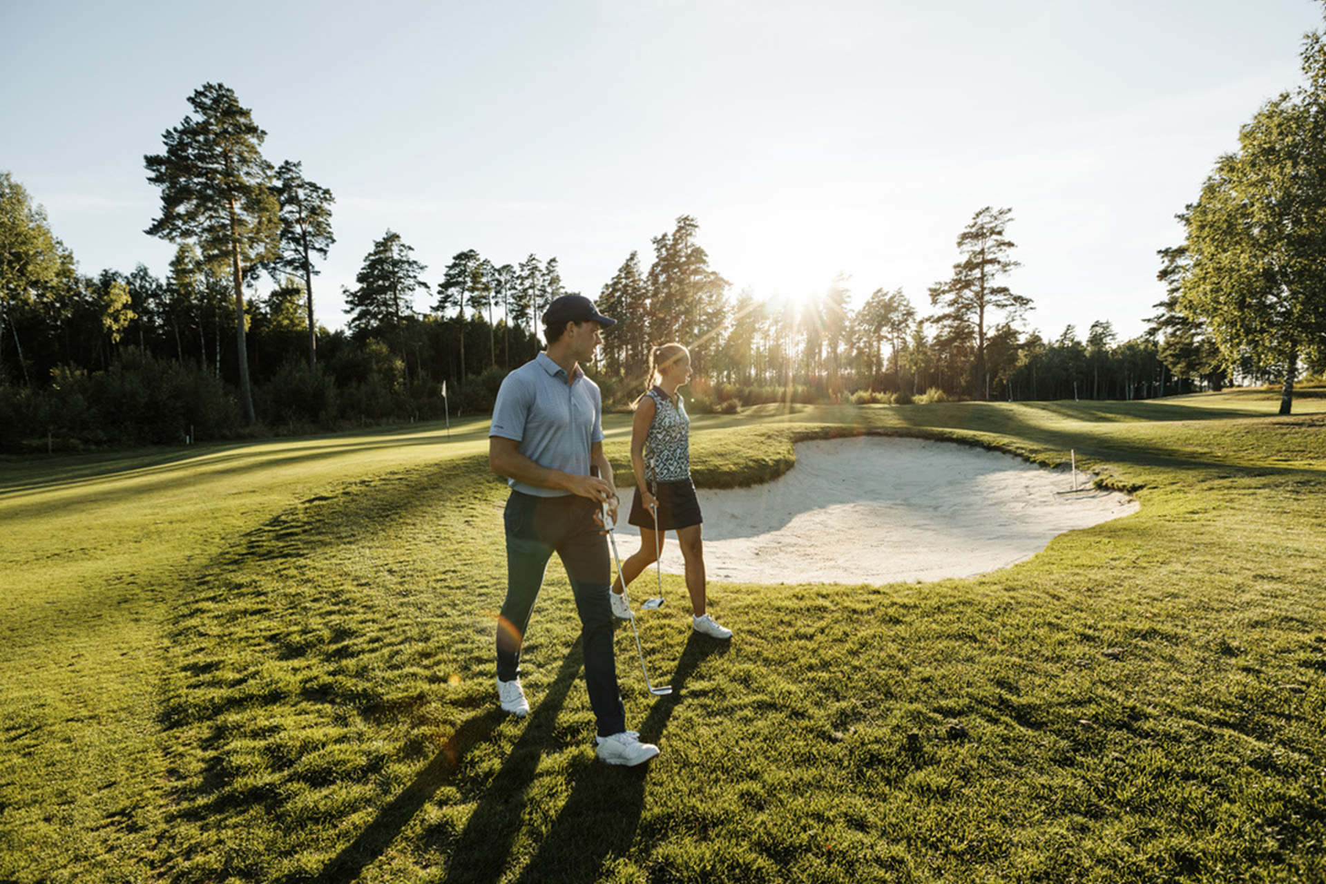 En kvinnlig och en manlig golfspelare går på golfbanan i motljus. Foto Henrik Mill.