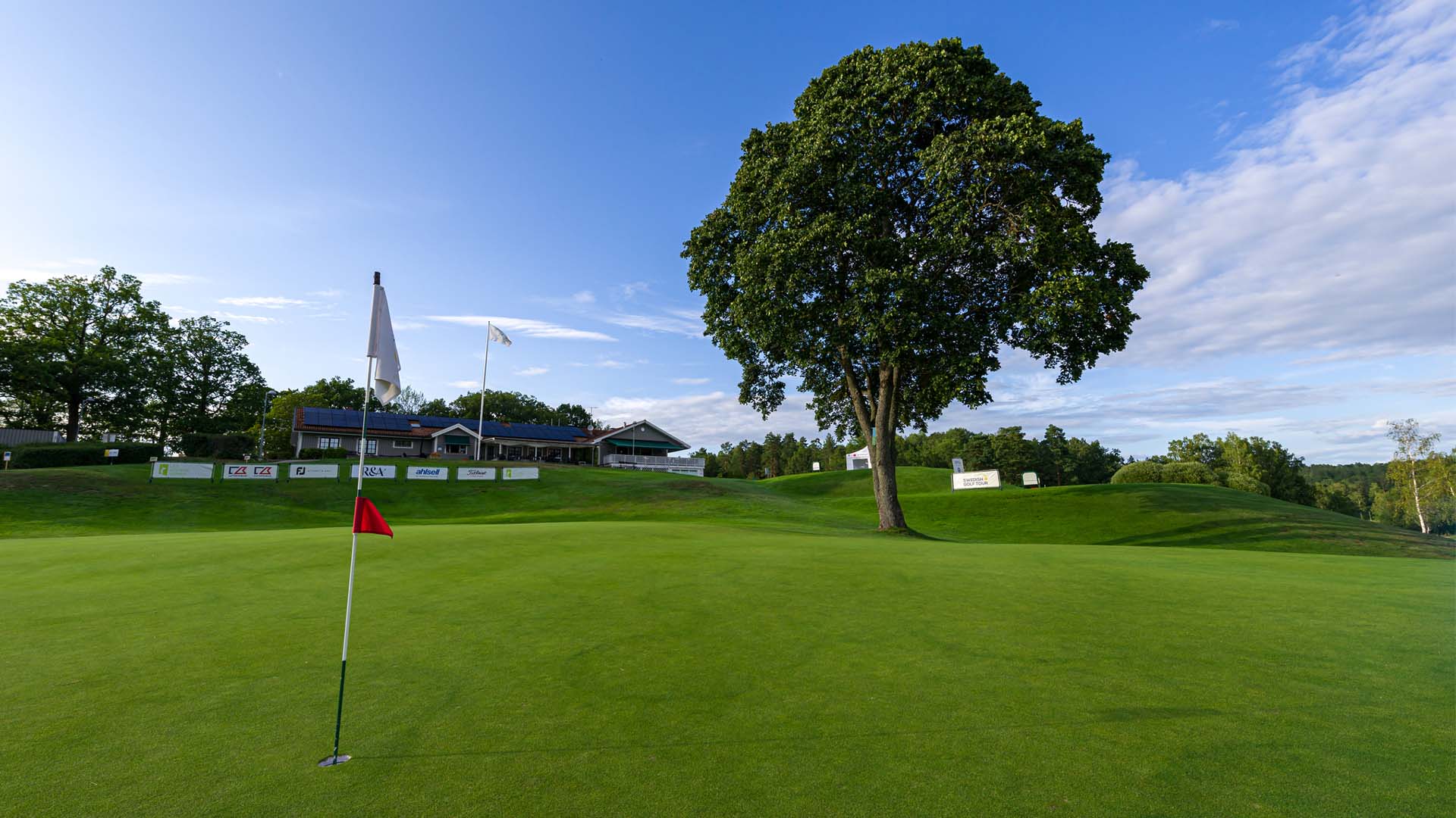 Vy över golfbana med klubbhuset i bakgrunden. Pressbild