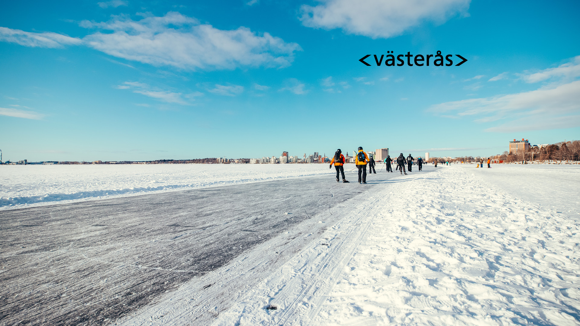 Vy över skridskoåkare på ett fruset Mälaren med Västerås i bakgrund. Foto: Avig Photo.