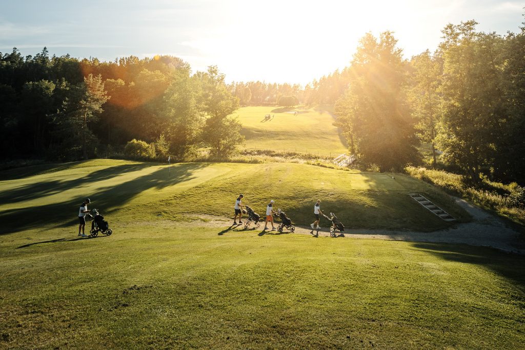 Kompisgäng som går med varsin golfvagn på en golfbana i Västmanland.