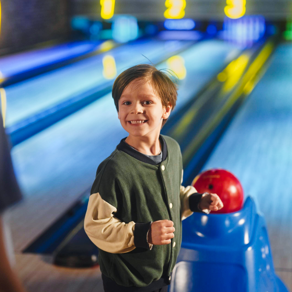 En glad pojke står med ett bowlingklot och ska spela bowling