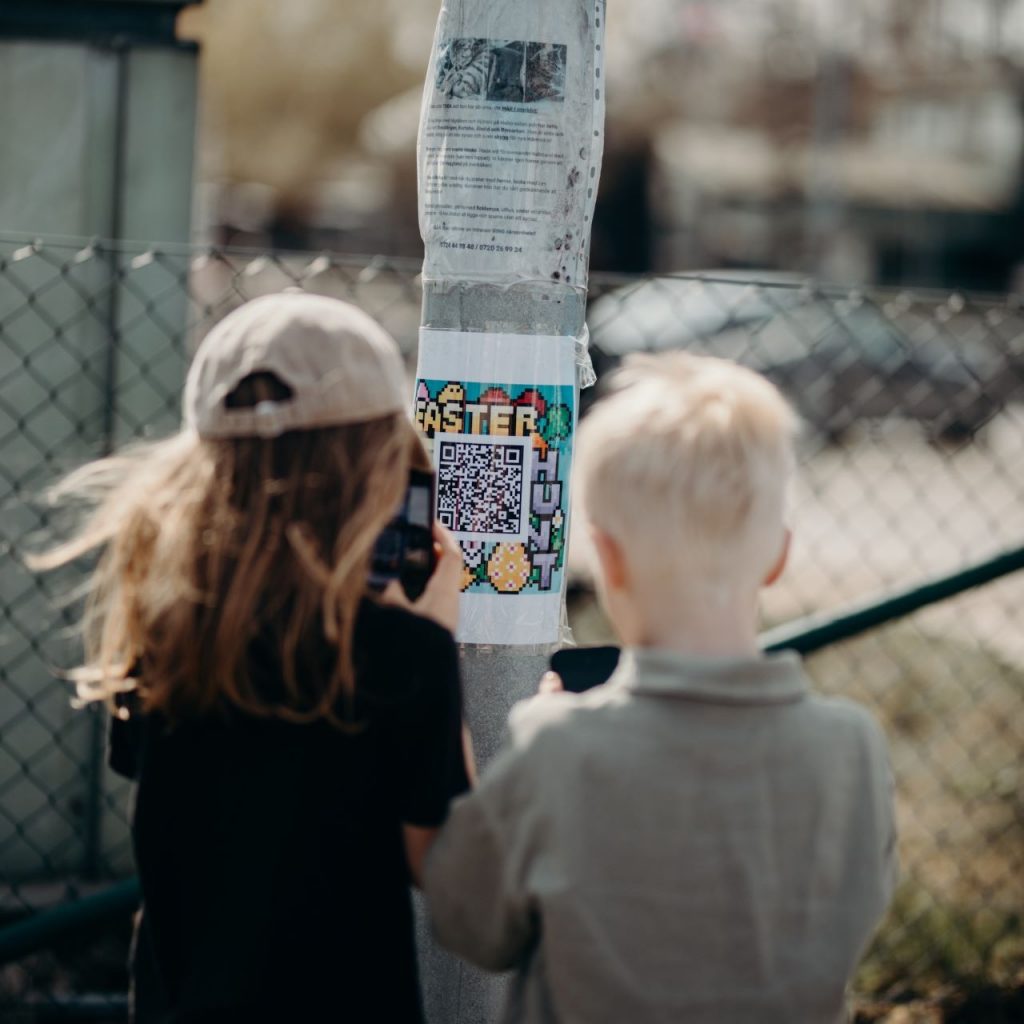 Två barn skannar en qr-kod på en lyktstolpe för att delta i en digital äggjakt.