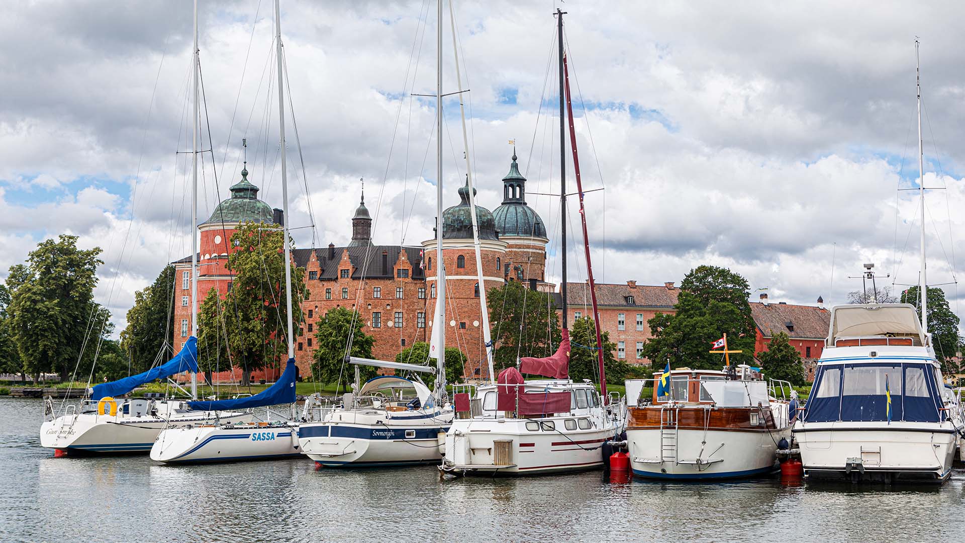 Båtar som ligger längs en brygga framför Gripsholms slott med sina torn i bakgrunden. Foto YAH.