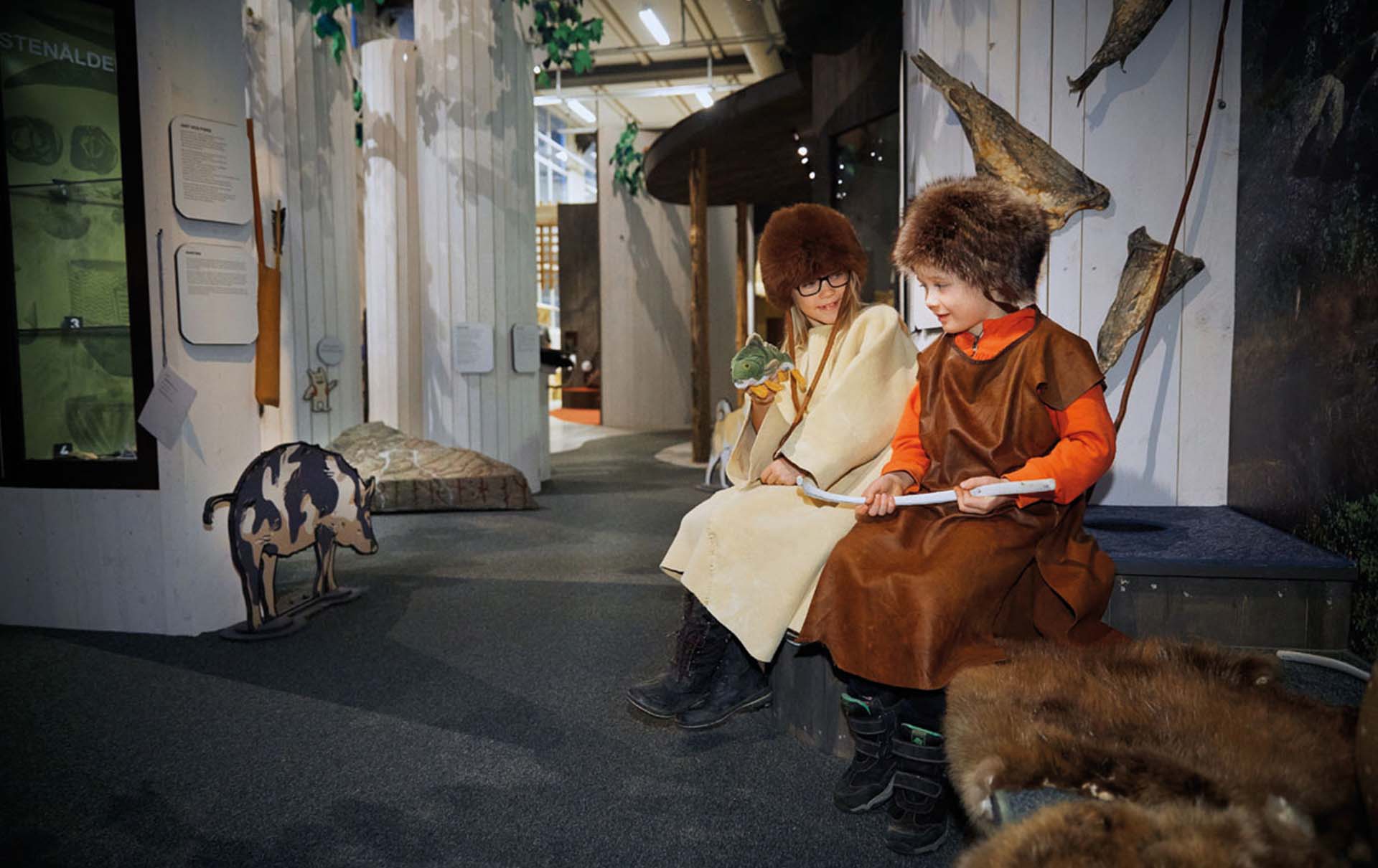 Två barn sitter i en museimiljö med tidsenliga kläder. Foto: Lasse Fredriksson.