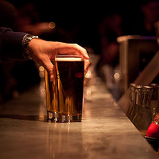 En hand ställer ner ett ölglas på bardisken. Foto mostphotos.