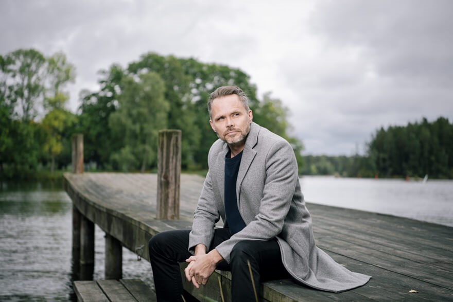 Konstnären Mikael Genberg sitter på en brygga iklädd grå kostym