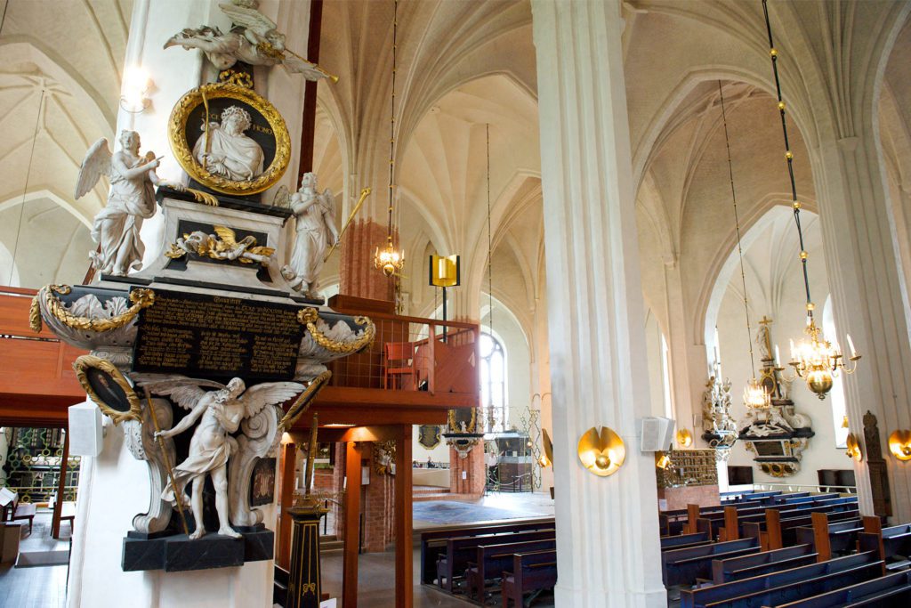 Interiör från Västerås domkyrka med ett epitafie i förgrunden och Erik IVXs sarkofag centrerad i bakgrunden.