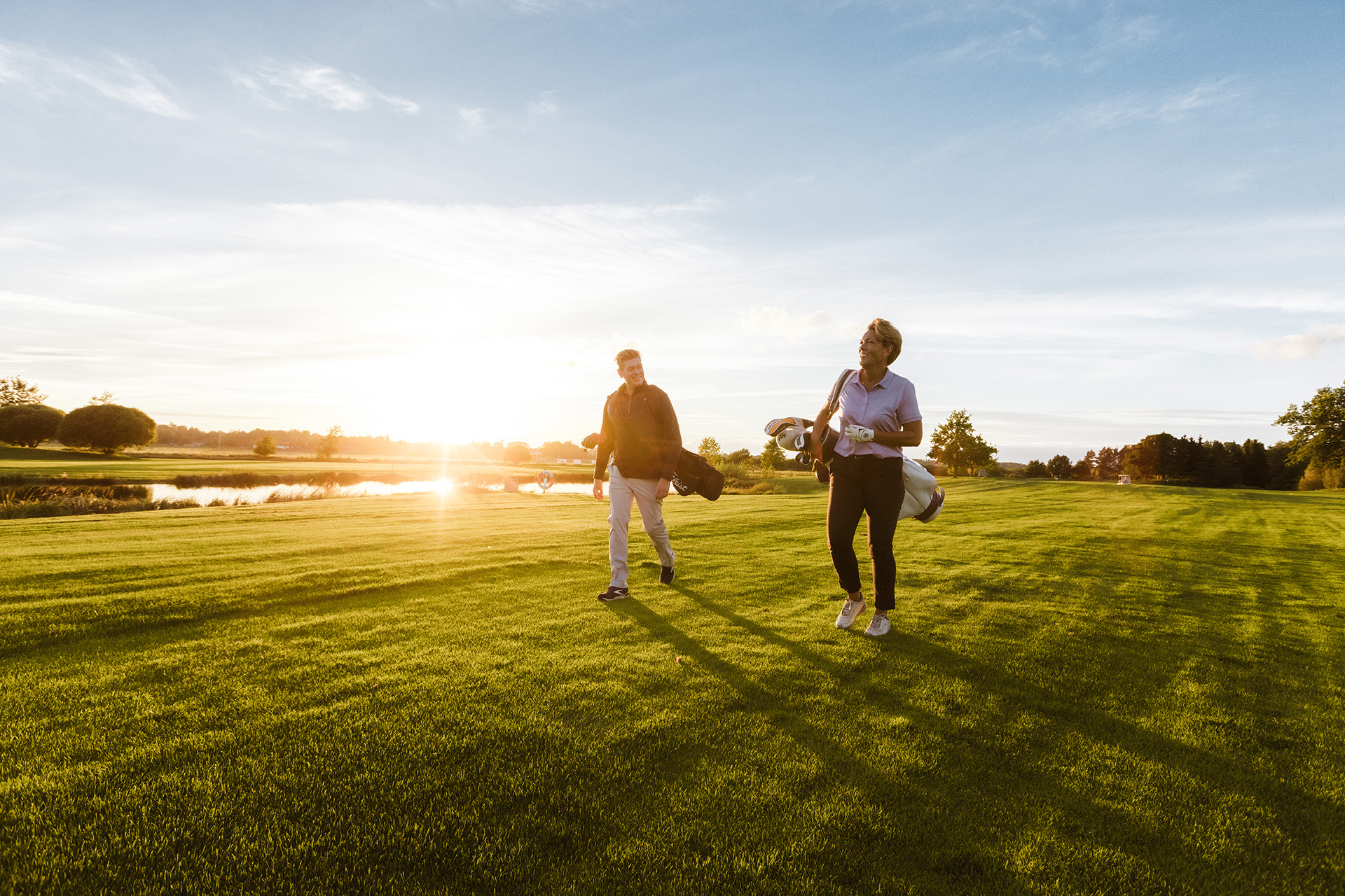 Två glada golfspelare går över en golfbana i motljus.