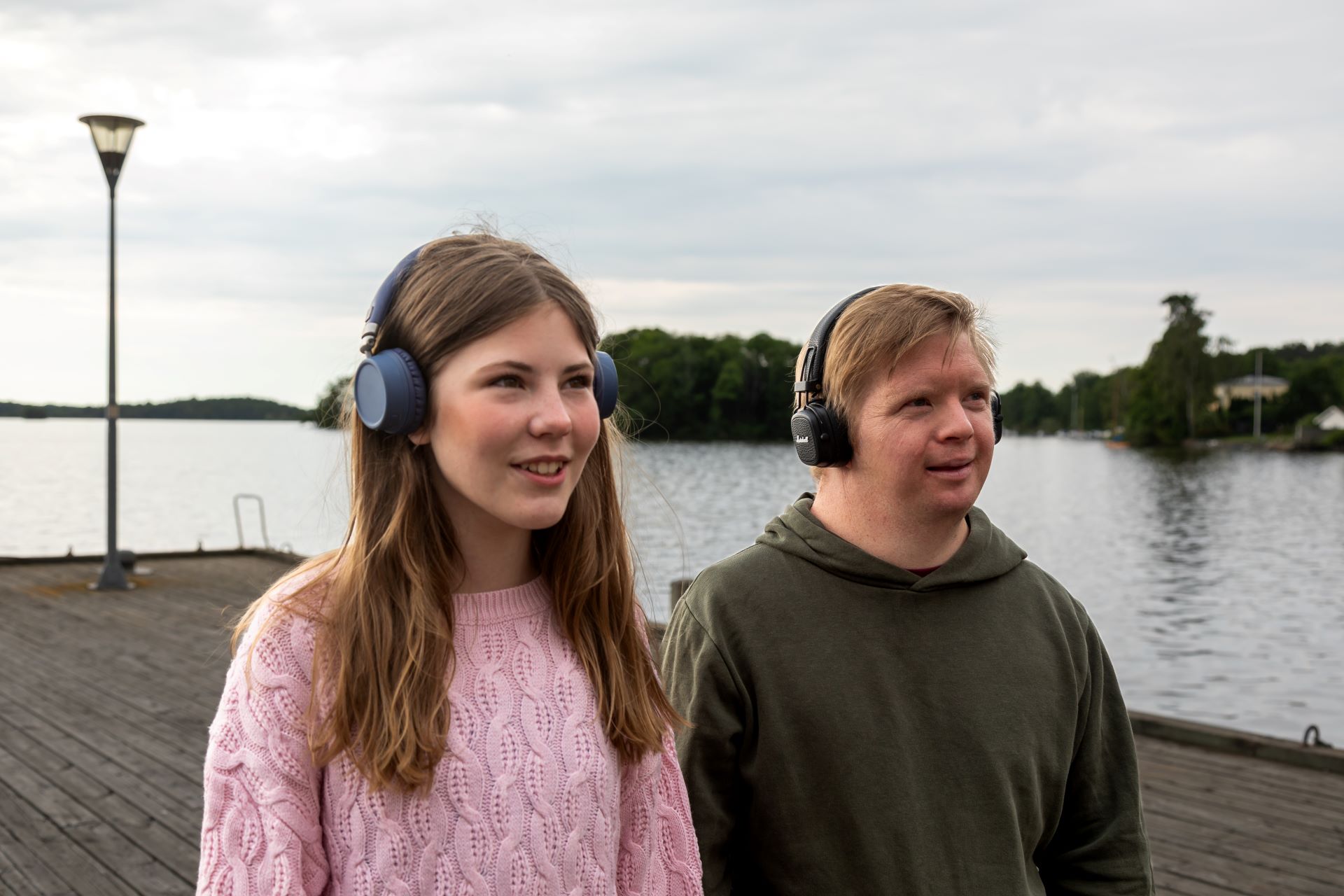 Två personer som går på en brygga i Strängnäs med hörlurar och lyssnar på en bokpromenad.