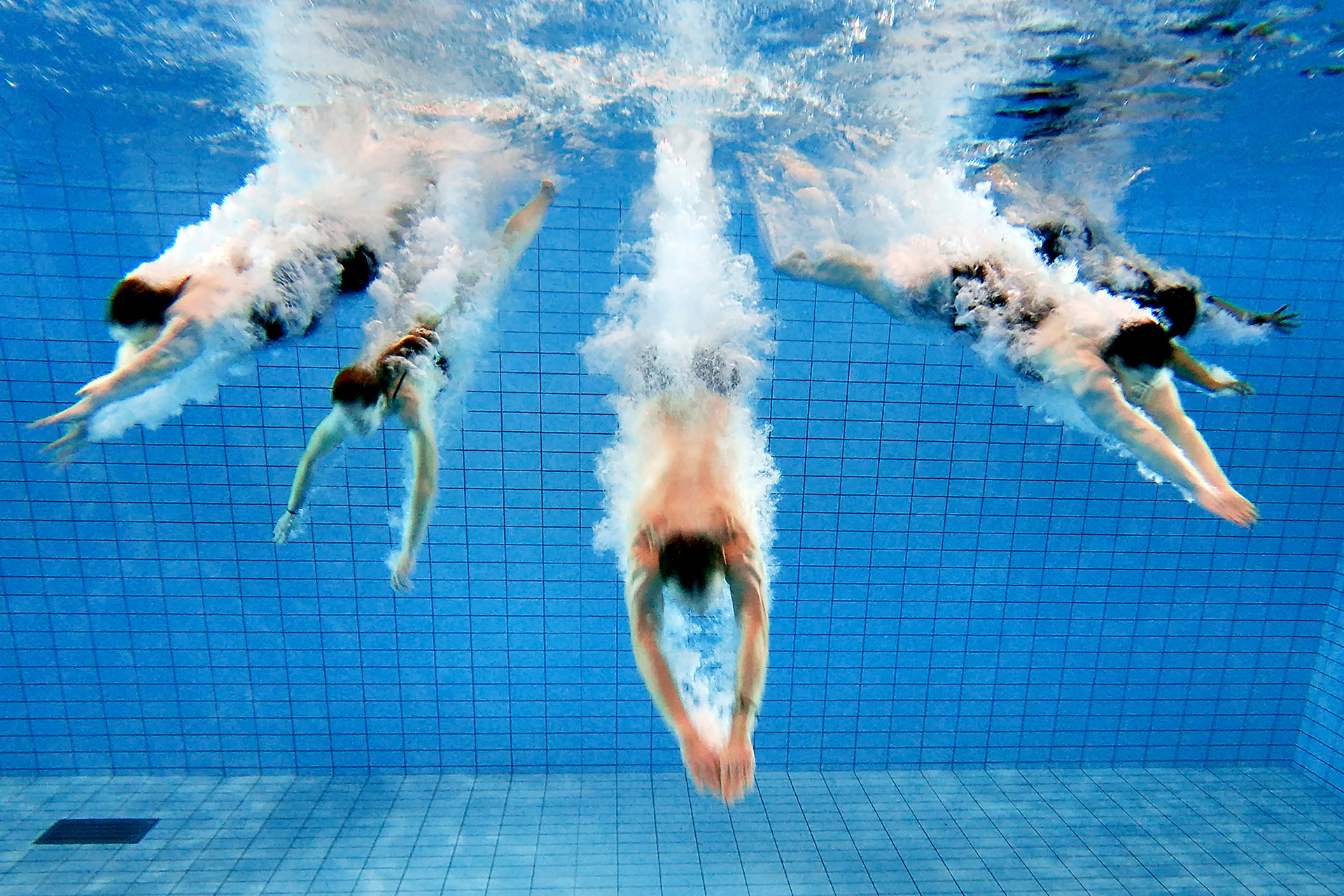 Fem personer dyker ner under vattnet i en pool.
