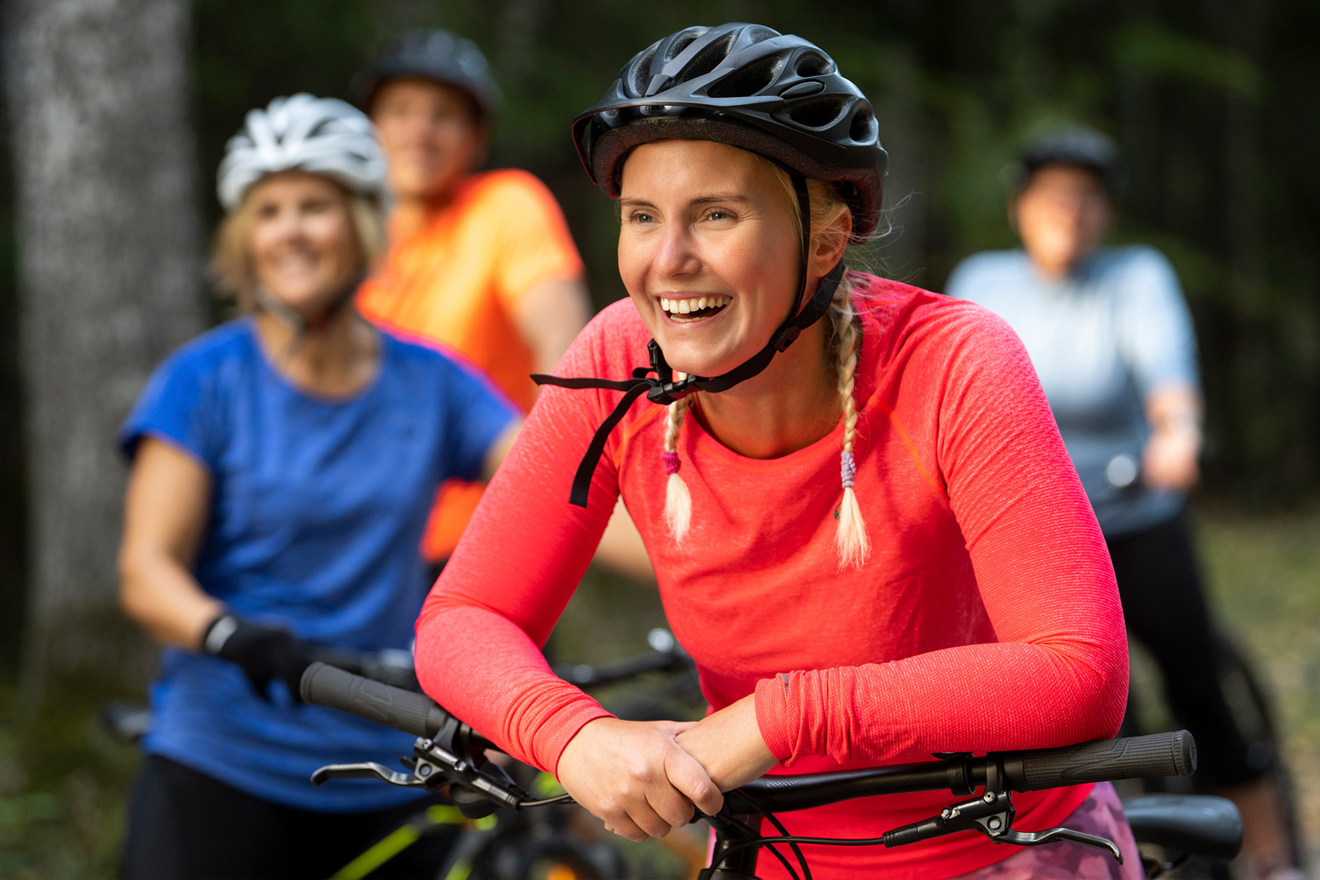 Ett gäng som pausar på en cykeltur, glad tjej med hjälm i förgrunden. Pressbild
