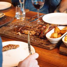 Måltid med kött, potatis och rödvin serverad på ett rustikt träbord i restaurangmiljö.