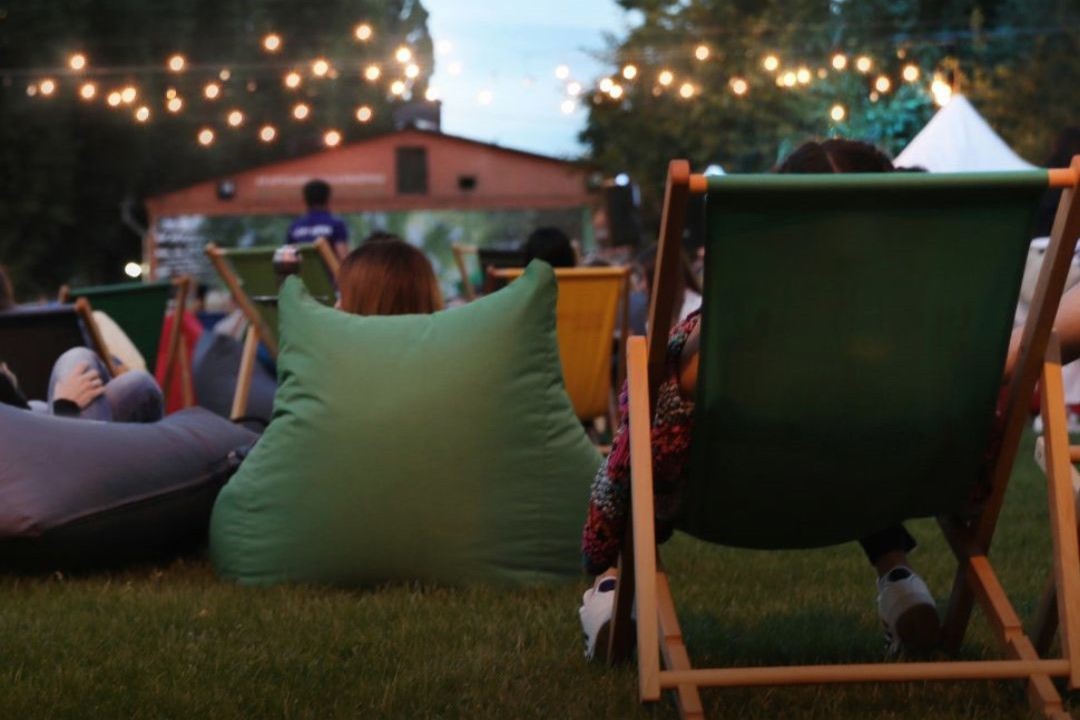 Publik som sitter i solstolar och på kuddar i en park och tittar på utomhusbio