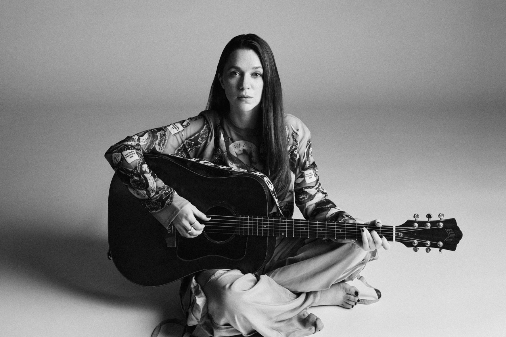 Pressbild på artisten Melissa Horn sittandes på golvet med en gitarr i knät