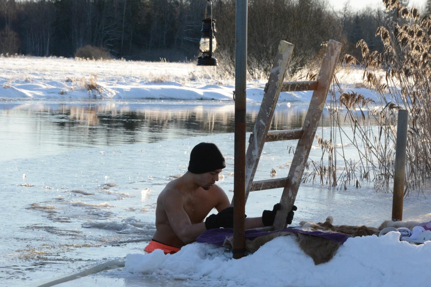 En man kliver ner från en stege i frusen sjö för att vinterbada