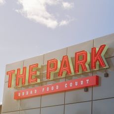 Fasad med The Park, Urban Food Court-skylt mot blå himmel.