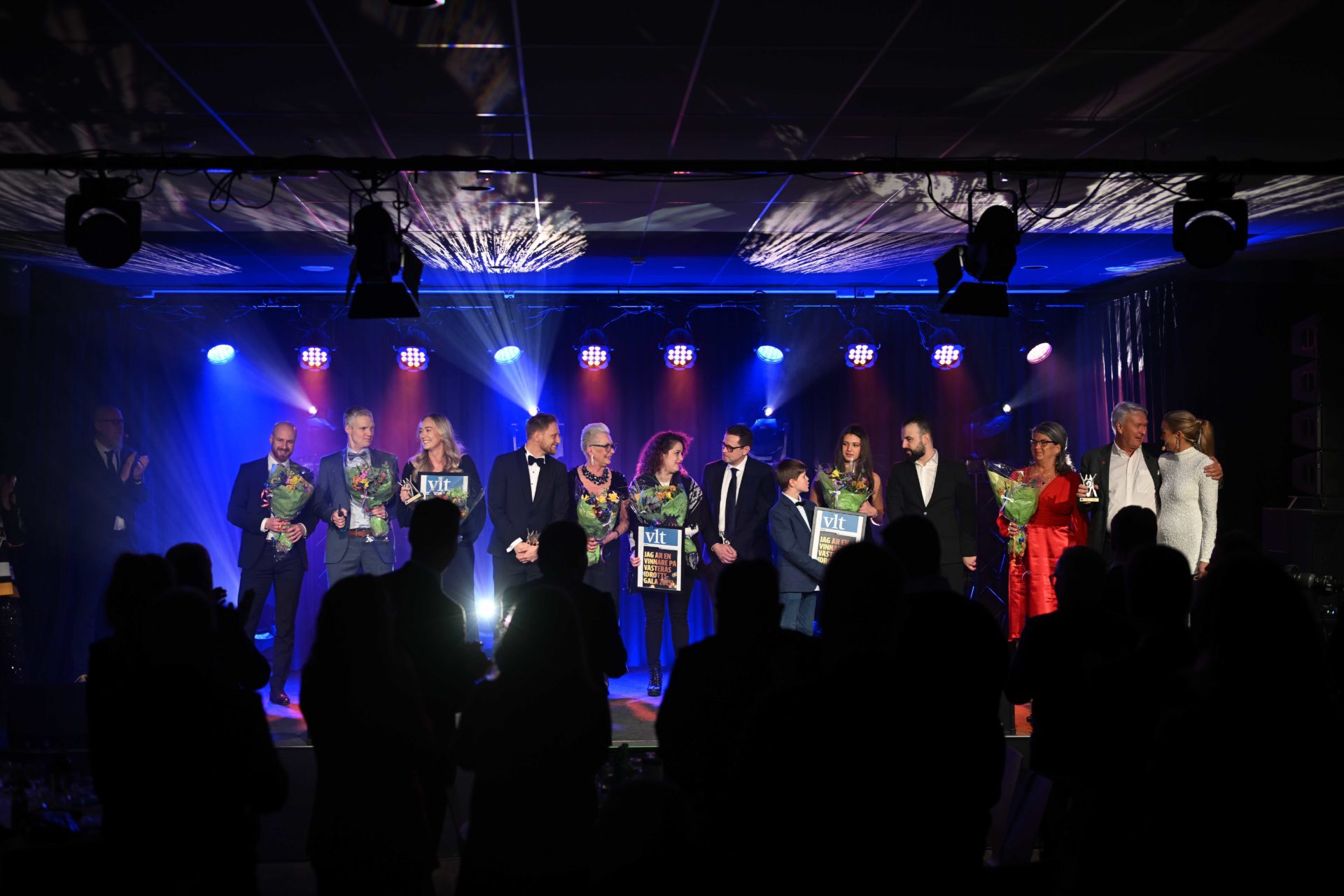 Pristagare står uppradade på scen under Västerås idrottsgala, med blommor och diplom i händerna.