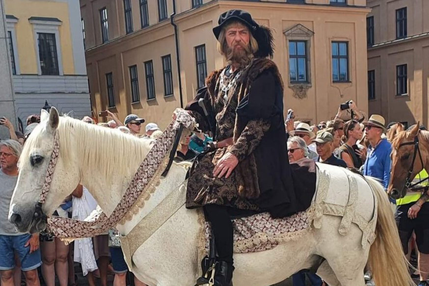 En man är utklädd till Gustav Vasa i tidsenliga kläder och rider på en vit häst.