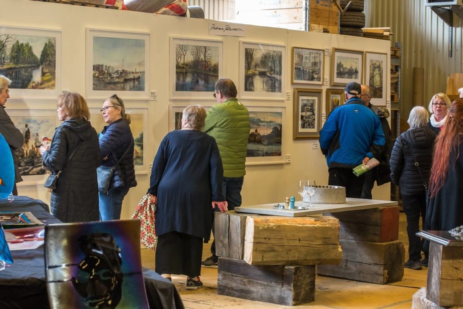 Flertal personer står och tittar på en vägg av konst, en bild från Konst och kulturrundan i Kolbäcksdalen