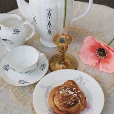 Uppdukat porslin, kanelbulle messingsstake och rosa blomma på Karlsgatan Kafé.