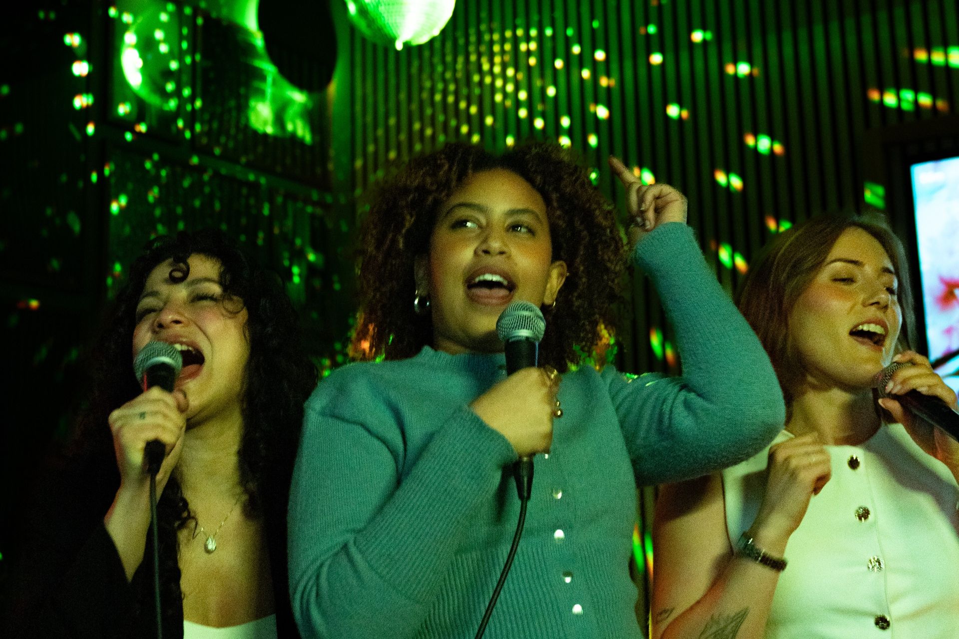 Tre tjejer som sjunger karaoke under en discokula på O'Learys.