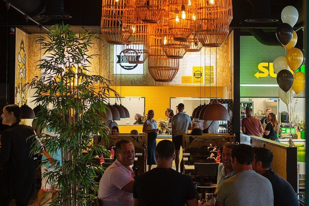 En grupp människor som sitter och äter framför Ribhaus och Subway inne på The Park Food Court.