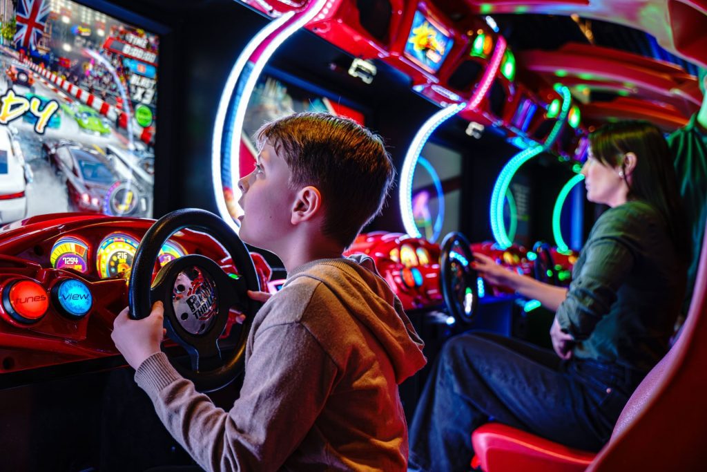 Ett barn och en kvinna sitter och spelar arkadspel med bilratt.